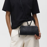 Person wearing a black t-shirt and light-colored pants holding a black crossbody bag against a white background
