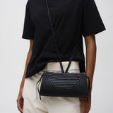 Person wearing a black t-shirt and light-colored pants with a black crossbody bag on a white background