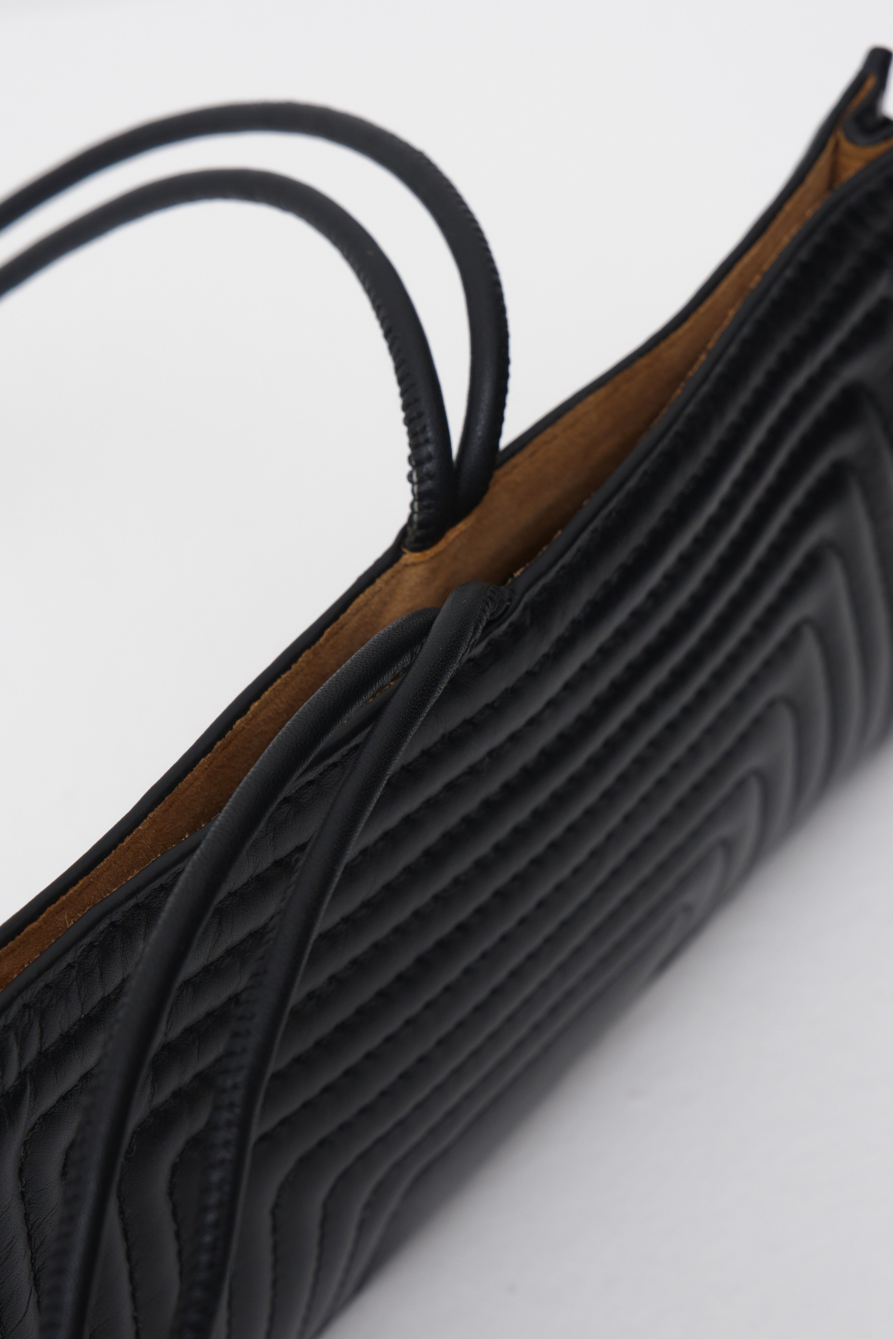 Close-up of a black textured crossbody bag on a light gray background