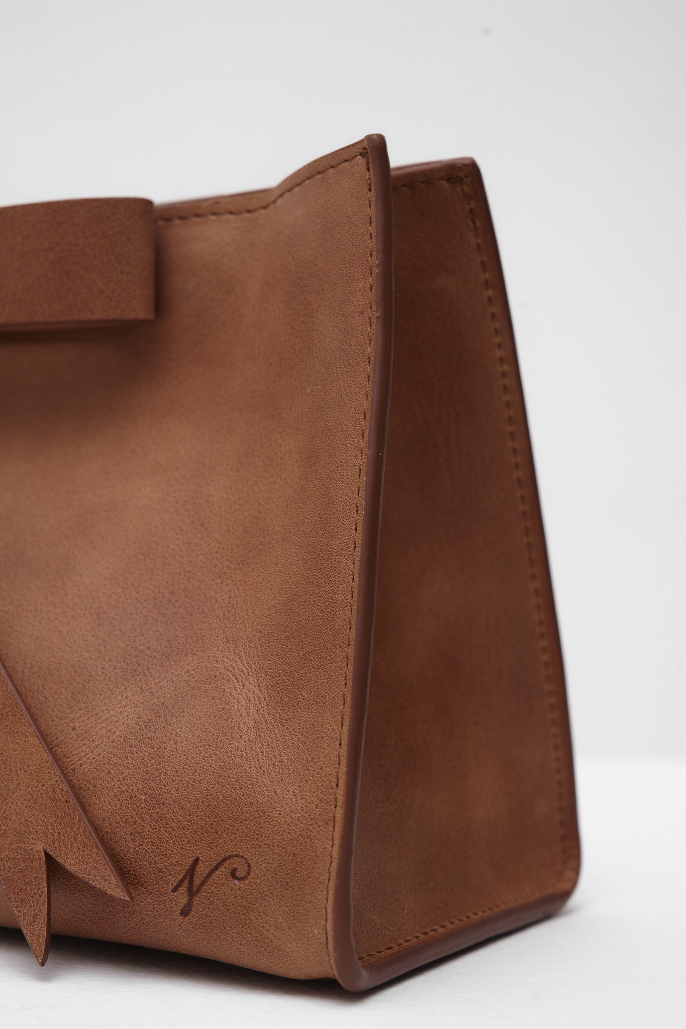Brown leather handbag with a bow on a white background
