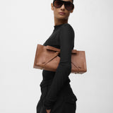 Woman holding a brown leather bag with a bow against a white background