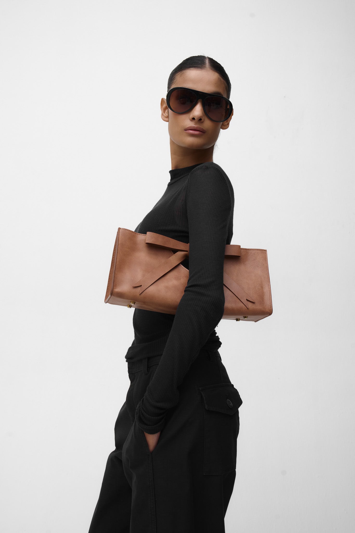 Woman holding a brown leather bag with a bow against a white background