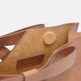 Close-up of a brown leather handbag with a visible brand label on a white background.