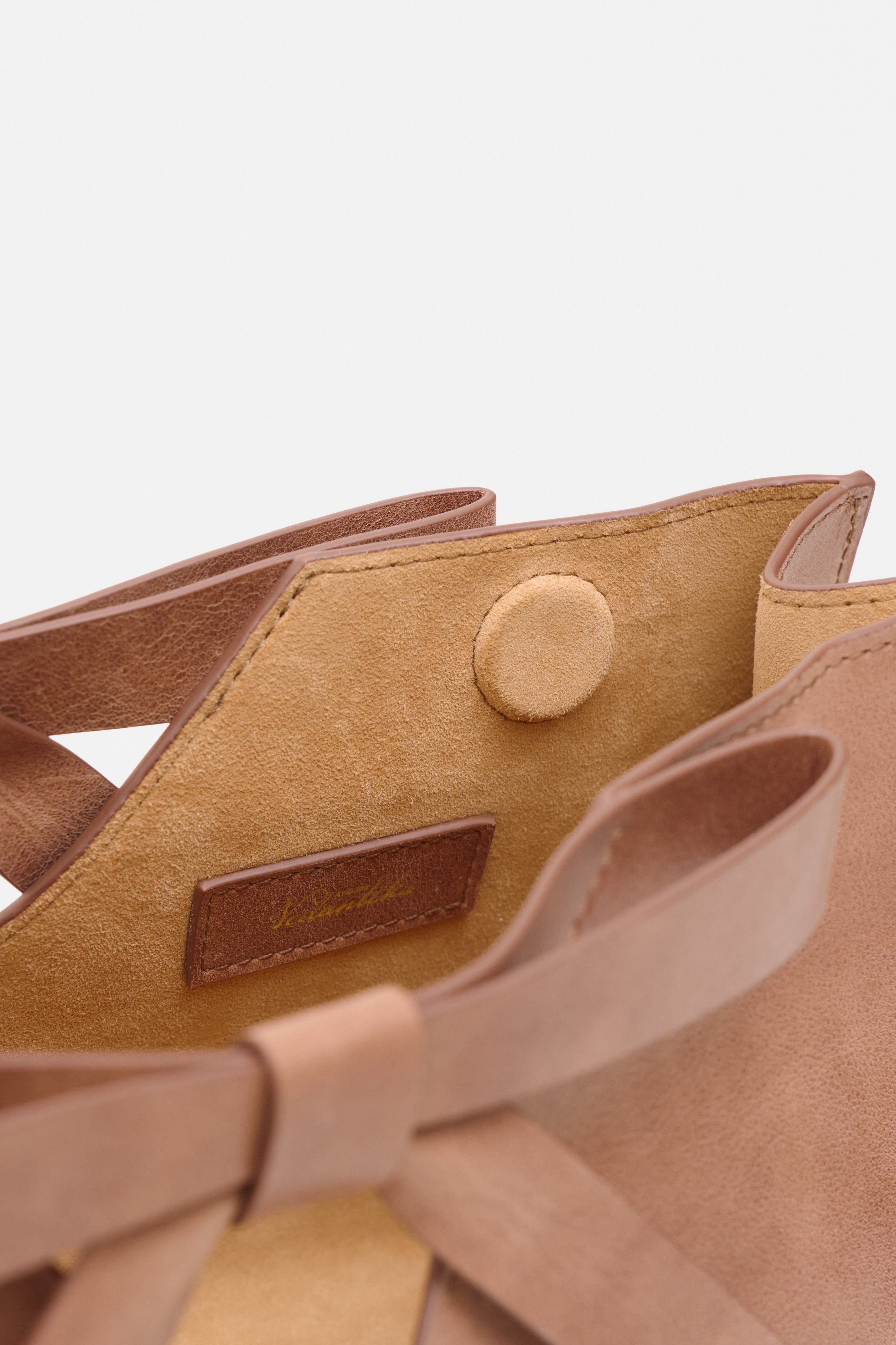 Close-up of a brown leather handbag with a visible brand label on a white background.