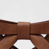 Close-up of a brown leather clutch bag with a bow detail on a white background