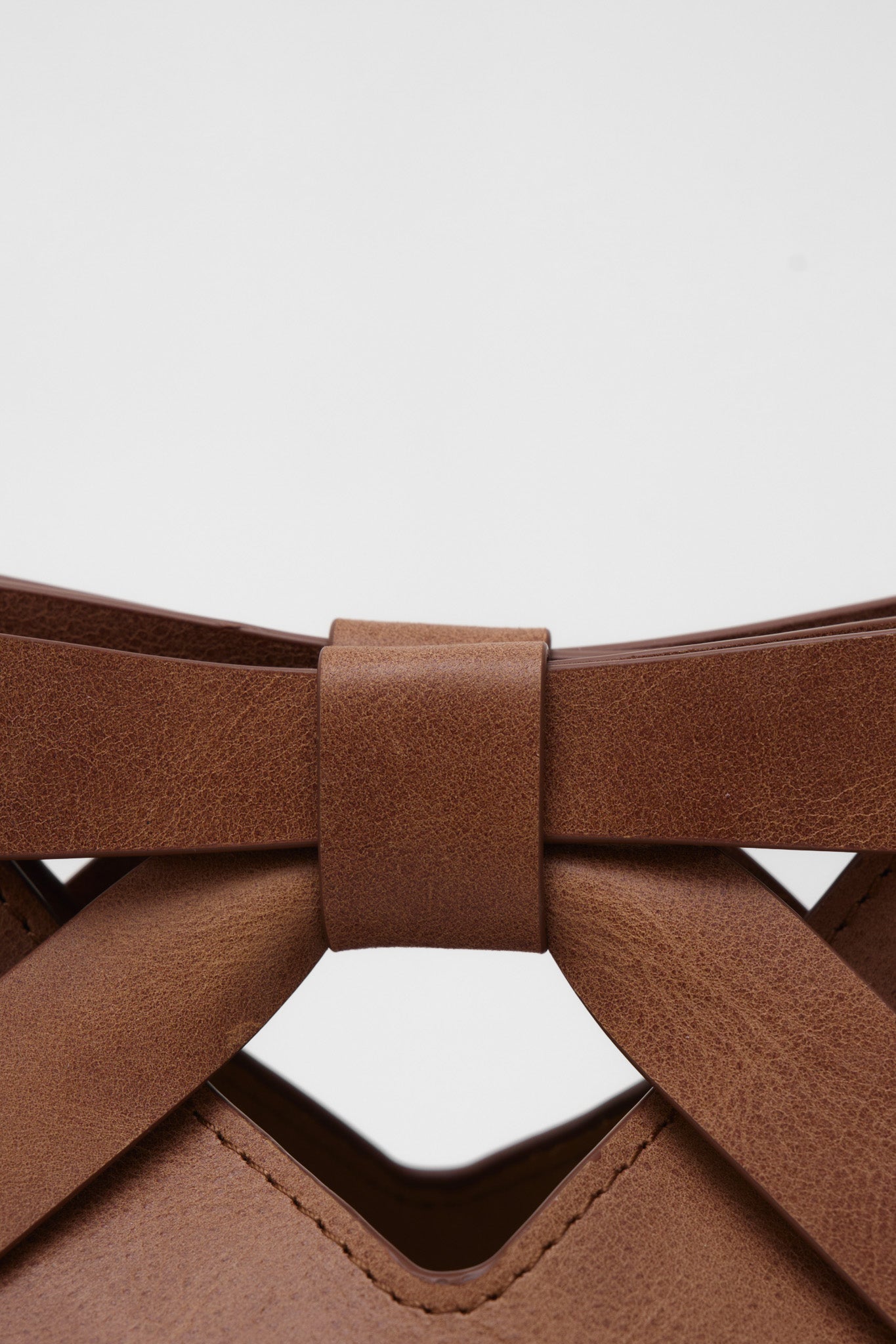 Close-up of a brown leather clutch bag with a bow detail on a white background