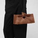 Woman holding a brown leather clutch bag with a bow against a plain background