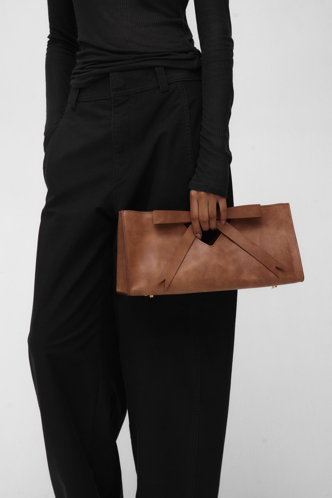 Woman holding a brown leather clutch bag with a bow against a plain background