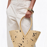 Person holding a beige handbag with black spots against a white background