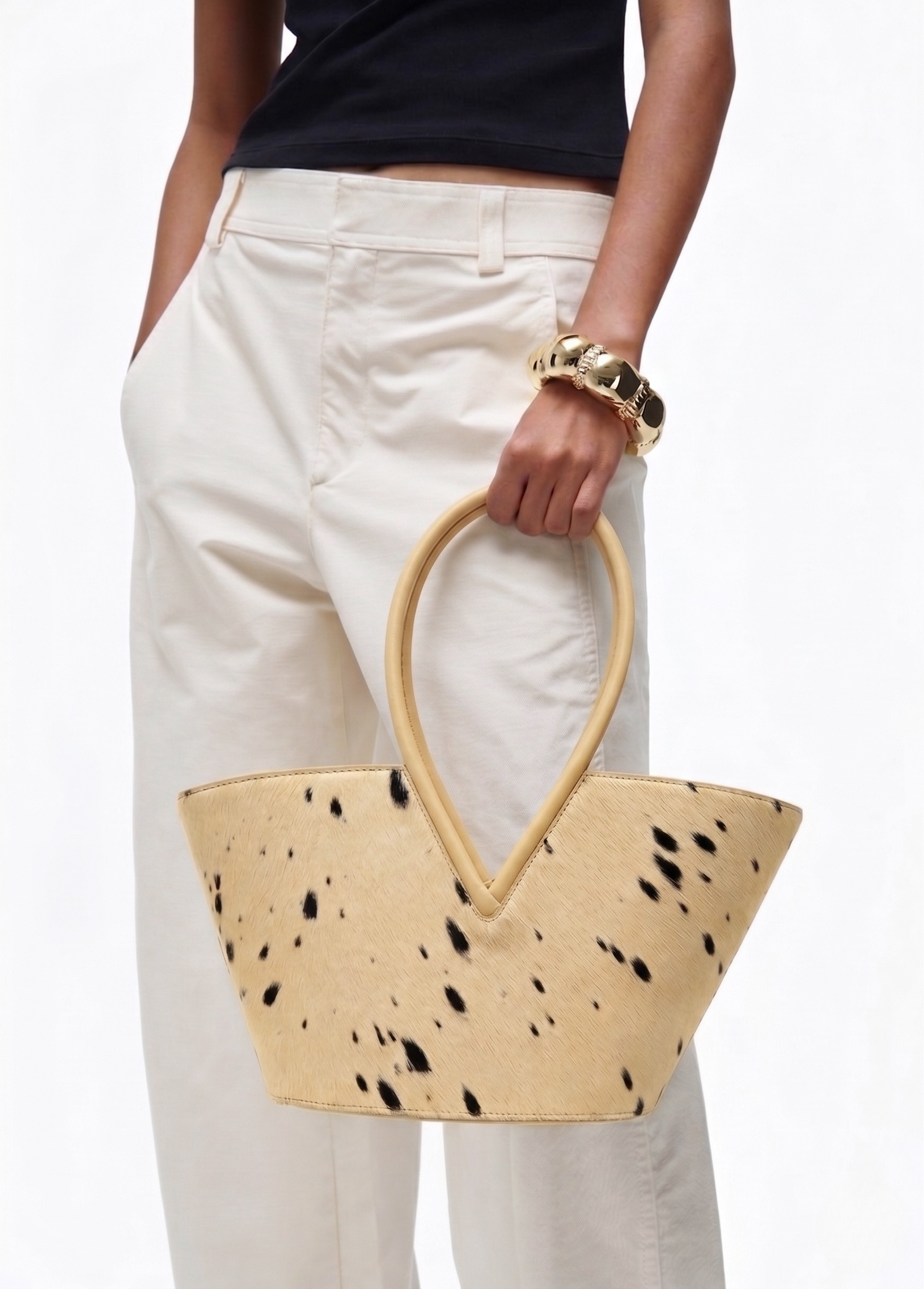 Person holding a beige handbag with black spots against a white background