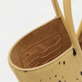 Close-up of a beige handbag with black speckles and brown interior on a white background