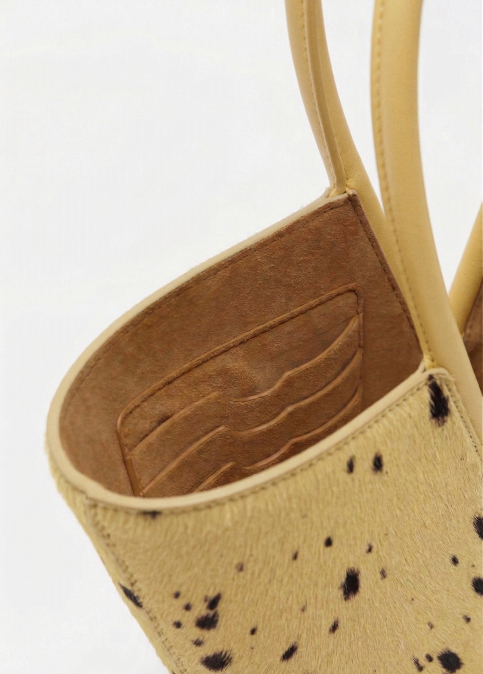 Close-up of a beige handbag with black speckles and brown interior on a white background