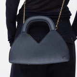 Person holding a navy blue handbag with a gold chain strap on a white background