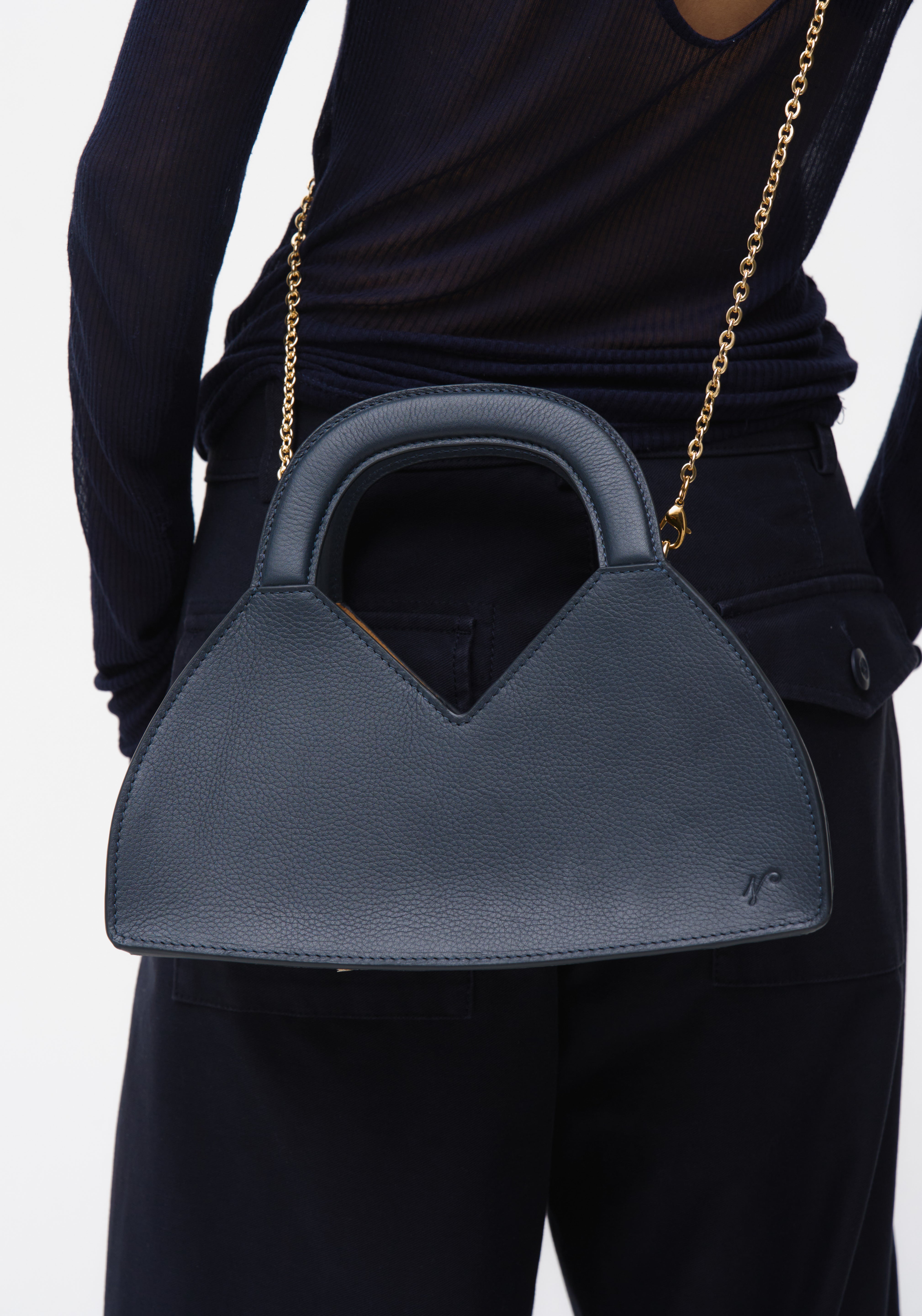 Person holding a navy blue handbag with a gold chain strap on a white background