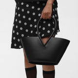 Woman wearing holding a black structured leather handbag on a white background