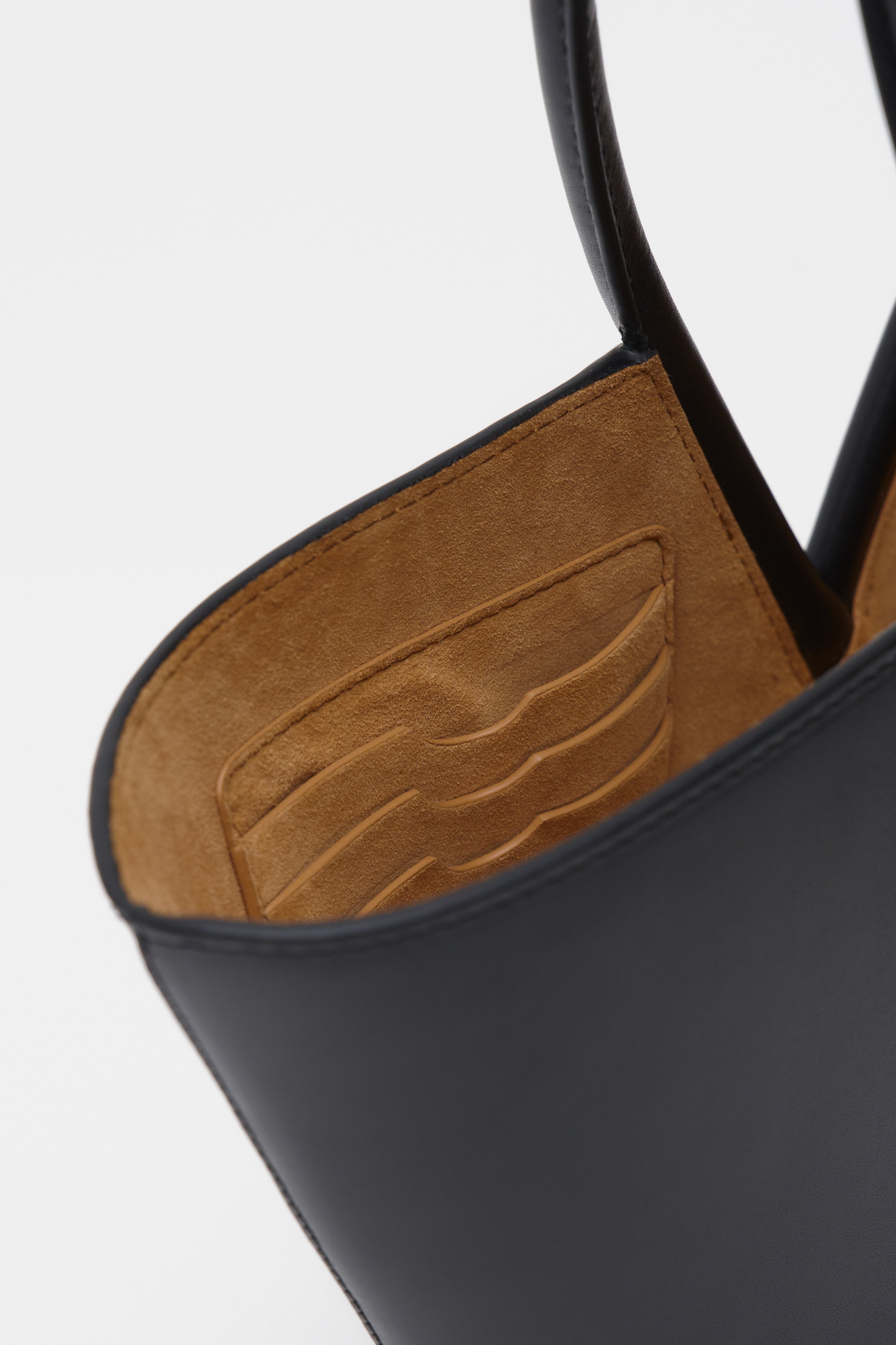 Close-up of a black leather handbag with brown suede interior on a white background